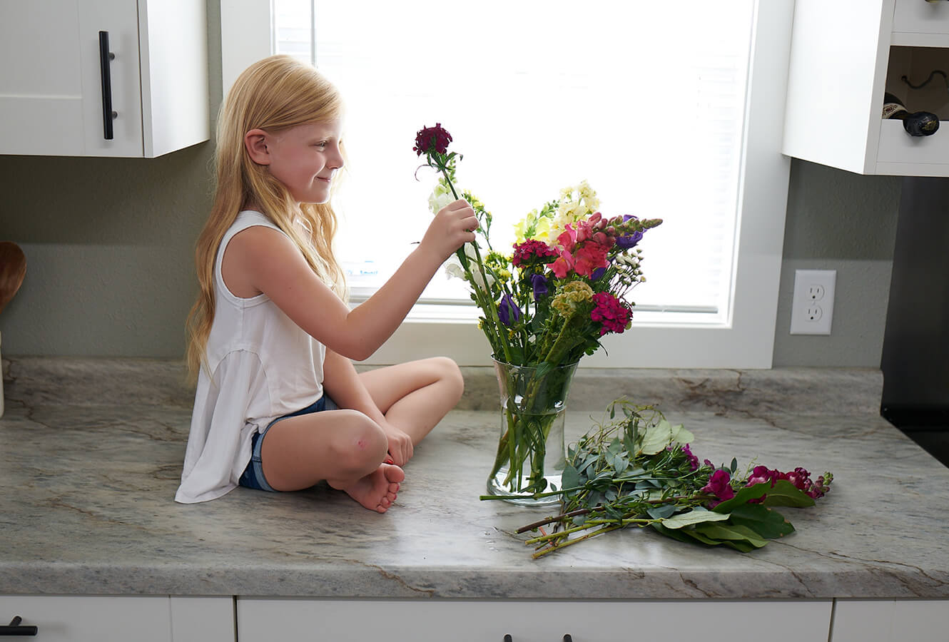 Kid Sitting On Counter With Flowers